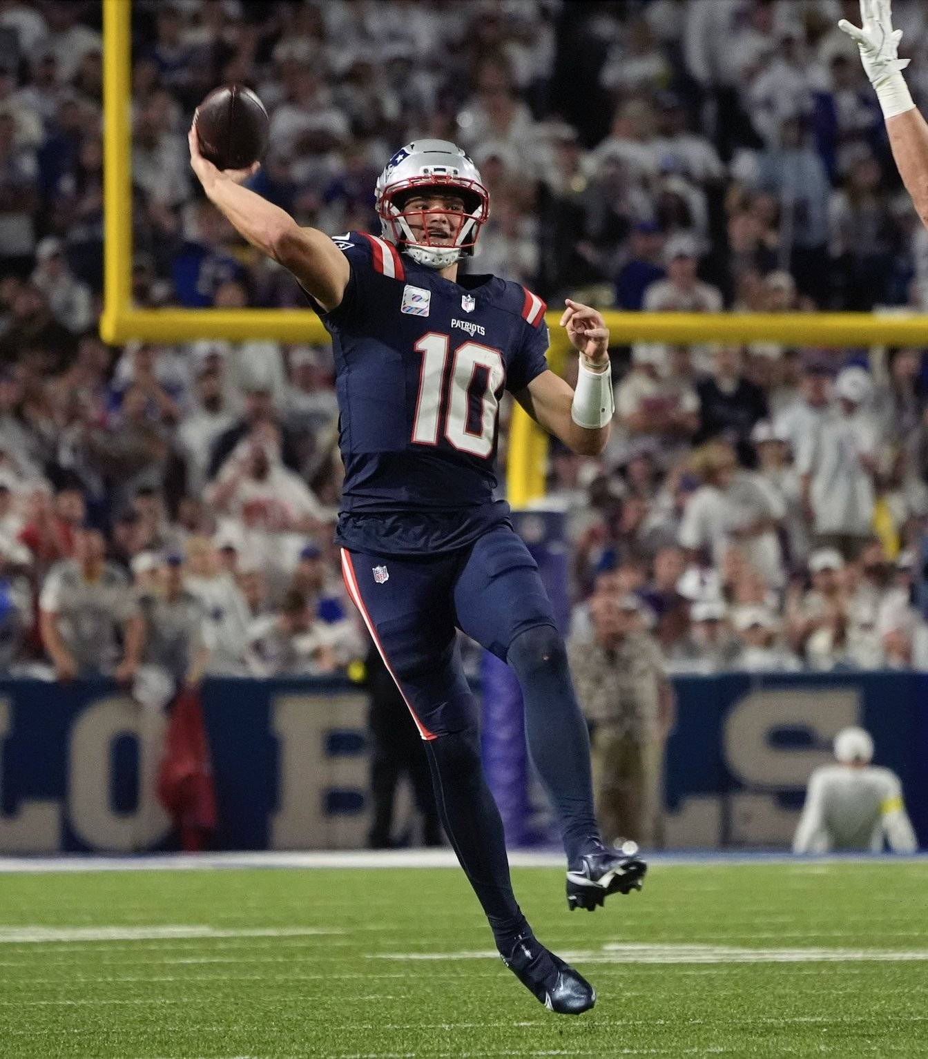 New England Patriots quarterback throws a pass during a night game as the crowd watches