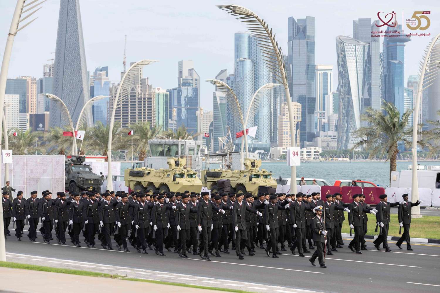 Marching units during the Qatar National Day Parade 2025 along Doha Corniche, with Doha skyline in the background