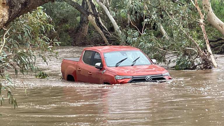 Red pickup truck stranded in floodwater in Queensland as monsoonal rains cause flooding across the region
