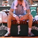 Jannik Sinner resting courtside with a towel during a hot French Open match.