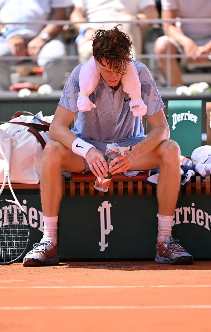 Jannik Sinner resting courtside with a towel during a hot French Open match.