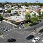Melbourne suburban neighbourhood with residential homes and a busy multi-lane road intersection under clear daytime skies, illustrating the city's housing market.