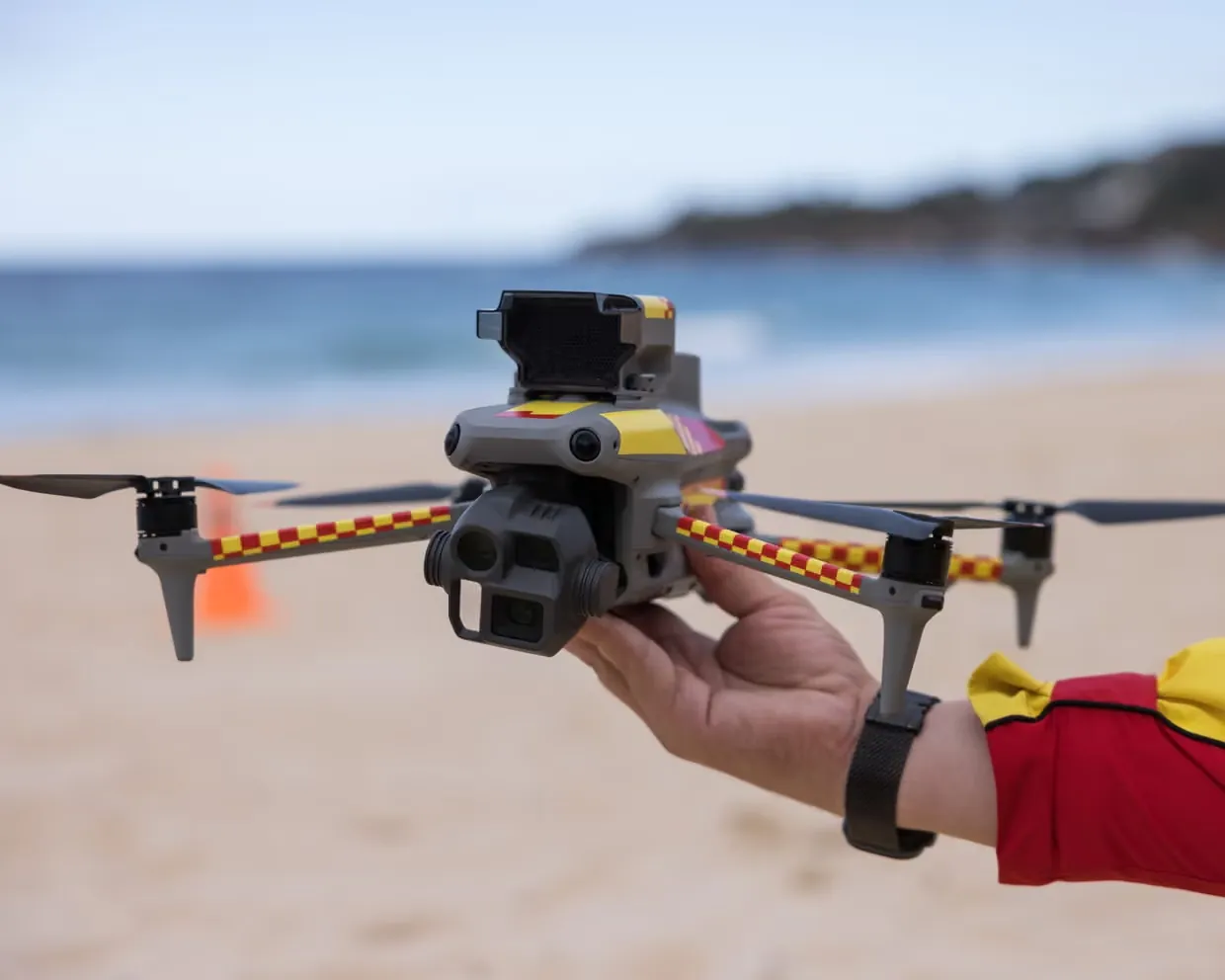 A Surf Life Saving NSW operator holds a shark-spotting drone on a beach as Australia expands year-round drone patrols across 70 NSW beaches under a $34 million shark safety program with AI detection trials