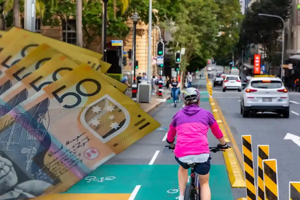 Cyclist riding in a Queensland bike lane with Australian $50 notes, illustrating Queensland's new e-bike laws, $518 fines, and road rule changes effective July 1, 2026.