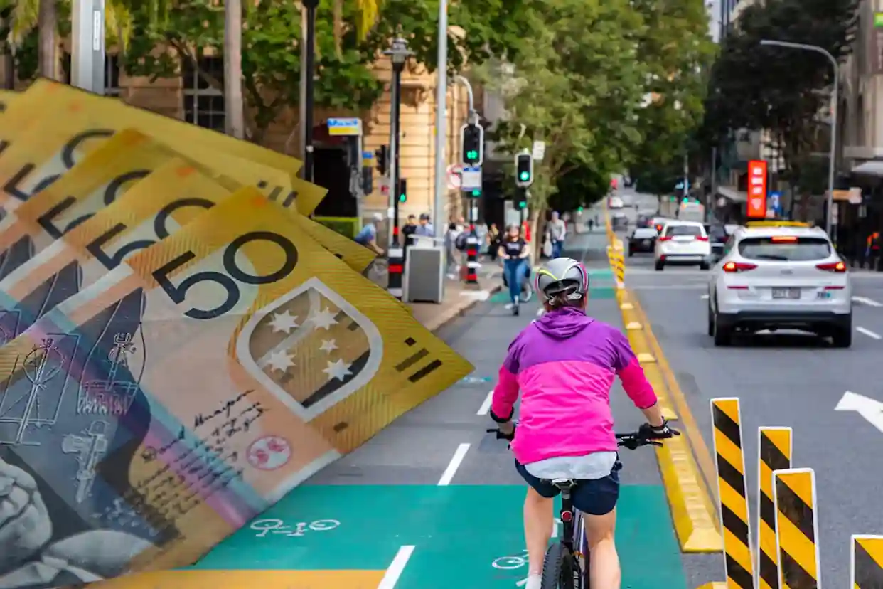 Cyclist riding in a Queensland bike lane with Australian $50 notes, illustrating Queensland's new e-bike laws, $518 fines, and road rule changes effective July 1, 2026.