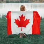 Person holding a Canadian flag beside a lakeside on Vancouver Island ahead of Canada Day 2026 celebrations.
