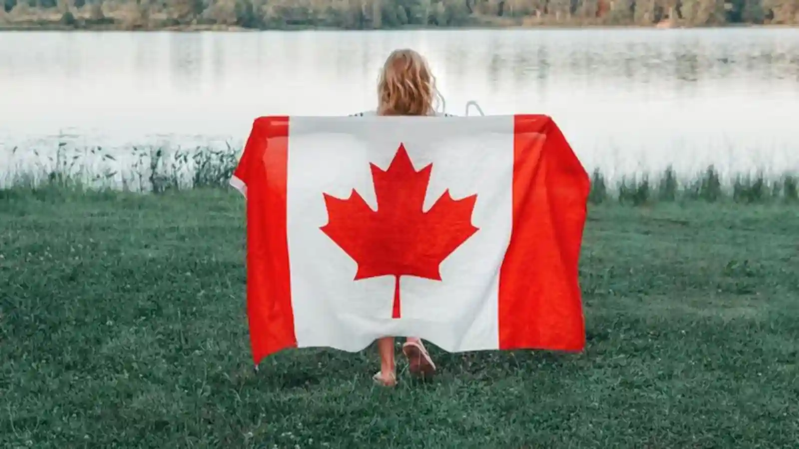 Person holding a Canadian flag beside a lakeside on Vancouver Island ahead of Canada Day 2026 celebrations.
