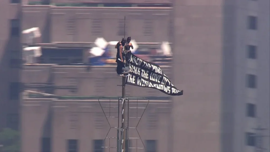 Two masked climbers stand atop the Empire State Building spire while unfurling a large peace banner high above Manhattan during an NYPD response in New York City on July 1, 2026.