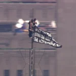 Two masked climbers stand atop the Empire State Building spire while unfurling a large peace banner high above Manhattan during an NYPD response in New York City on July 1, 2026.