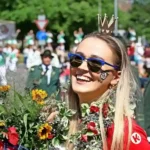Young woman wearing a ceremonial crown smiles while holding flowers during the Hannover Schützenfest Parade 2026 as marching bands and participants walk through Hanover city centre.