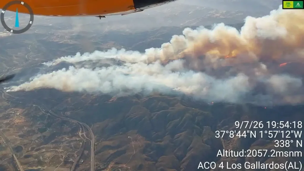 Aerial view of the fast-moving Los Gallardos wildfire in AlmerĂa, Spain, with thick smoke billowing over hills as firefighting aircraft monitor the blaze.