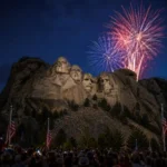 Mount Rushmore illuminated during the America 250 celebration with fireworks lighting the night sky as crowds gather for President Trump's July 3, 2026 event.