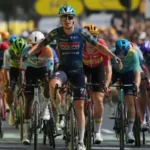Tim Merlier celebrates winning Stage 8 of the 2026 Tour de France in Bergerac as the peloton crosses the finish line behind him.