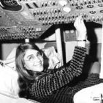 Margaret Hamilton-inspired Apollo software engineer beside stacks of flight code in a 1960s computer laboratory