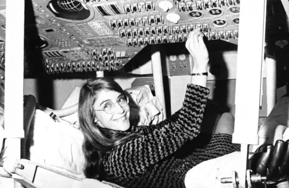 Margaret Hamilton-inspired Apollo software engineer beside stacks of flight code in a 1960s computer laboratory